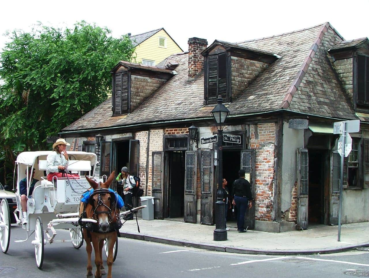 A horse drawn carriage riding past an old-timey bar in New Orleans