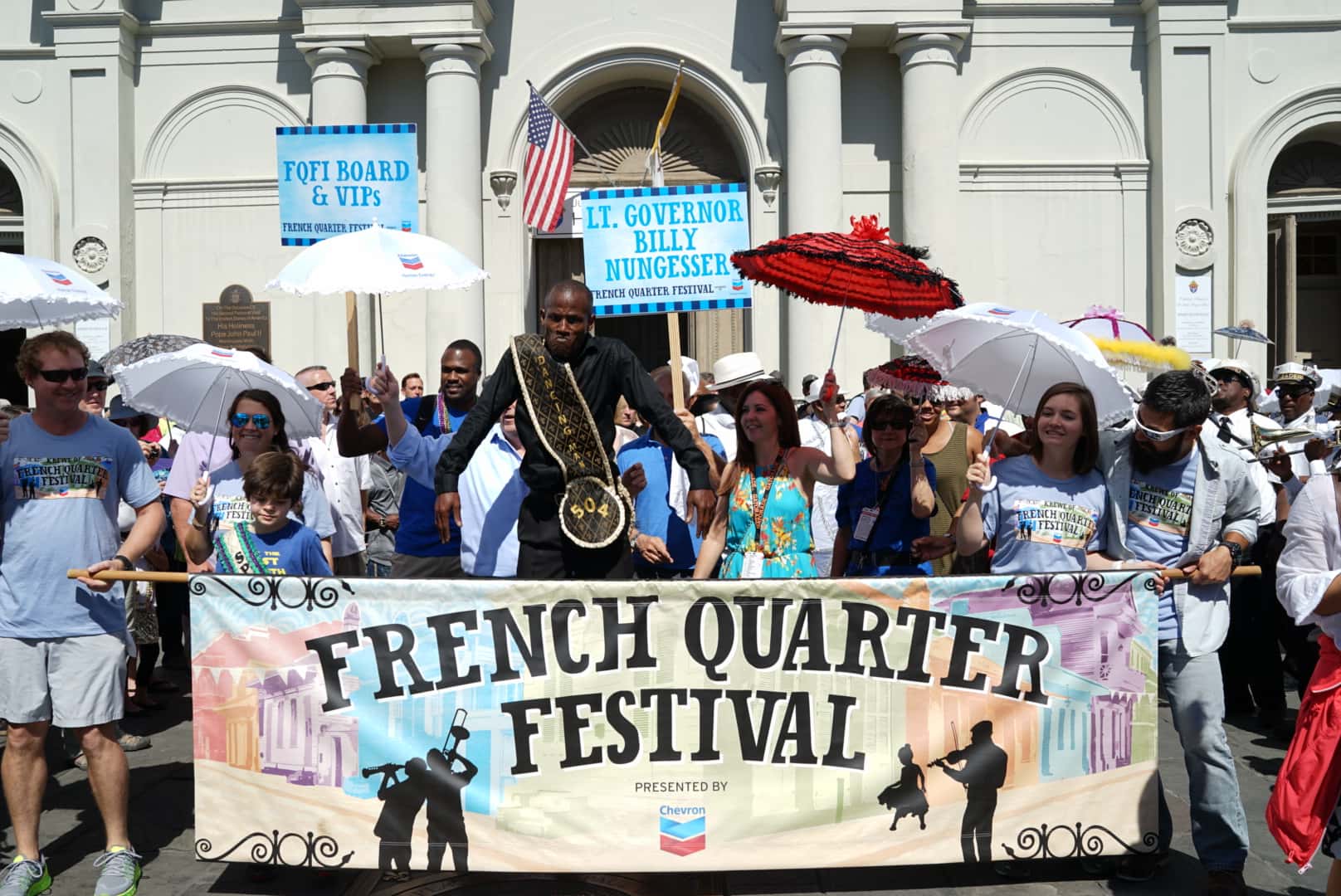 A small crowd holding a banner for the French Quarter Festival in New Orleans.